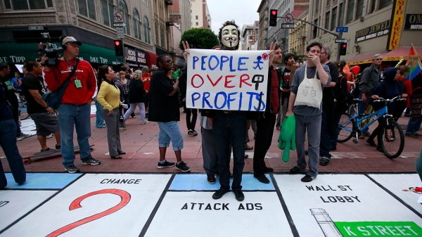 A protestor stands on a mock Monopoly game board on the street during May Day demonstrations in Los Angeles